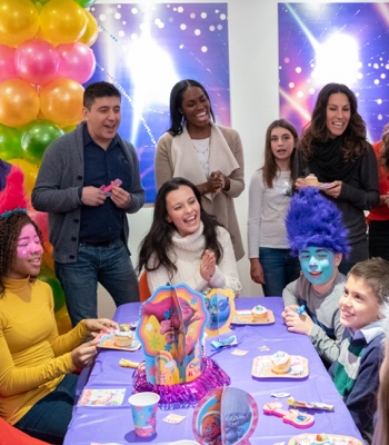Friends and family gather around a table for a Trolls birthday party
